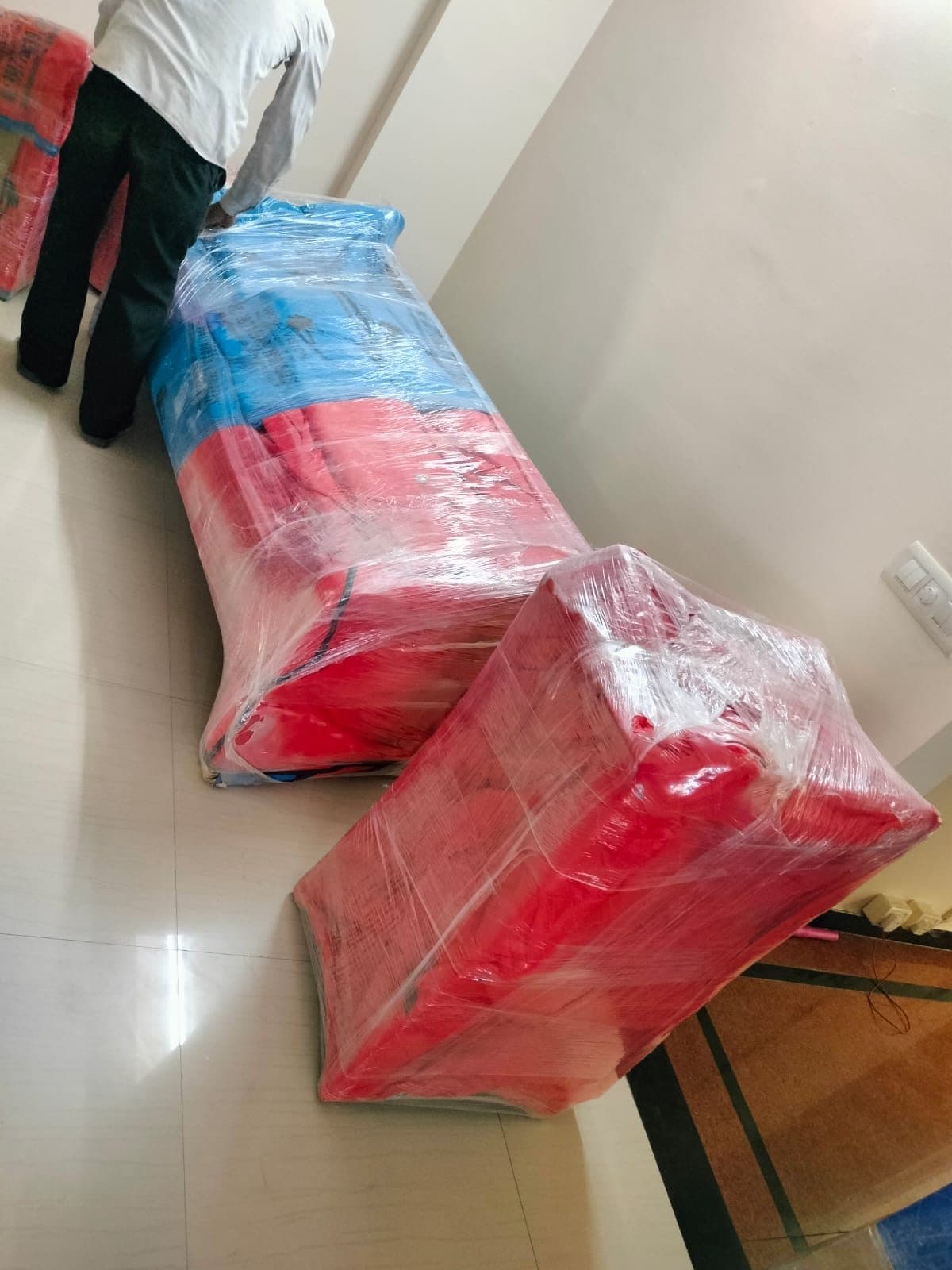 Mover carrying wrapped red and blue mattress bundles down a hallway