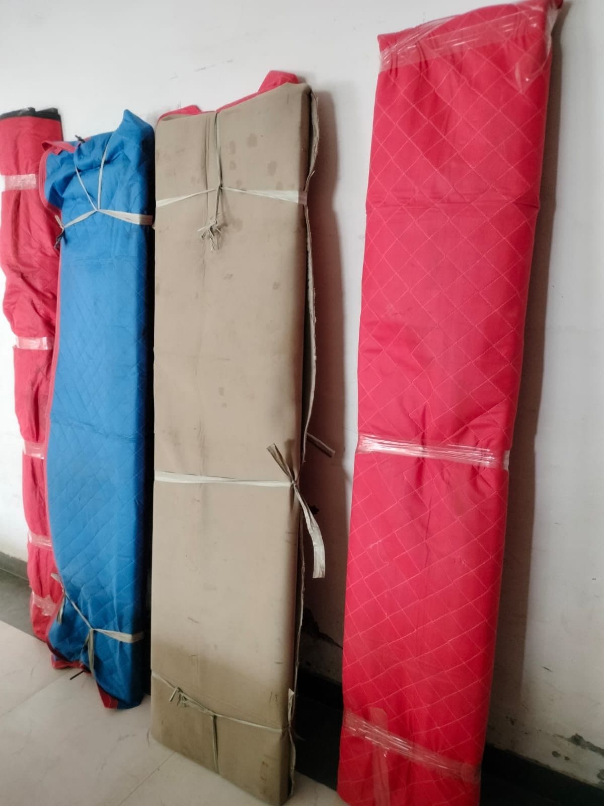 Rolled mattresses and carpets wrapped in quilted covers and leaned against a wall