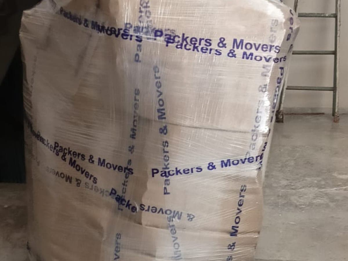 A large household bundle wrapped in stretch film and branded tape, staged by a staircase before loading