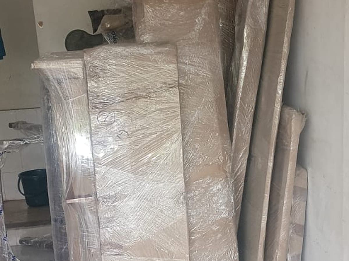 A wardrobe and long furniture pieces wrapped in stretch film and stood against a wall