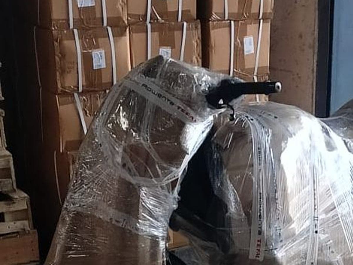 A motorcycle wrapped in stretch film beside packed cartons at a transport depot