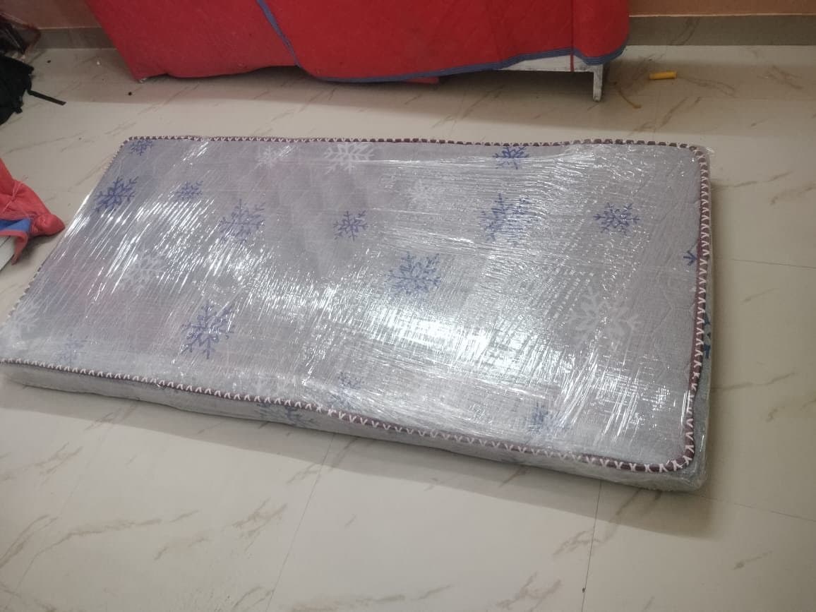 Single mattress wrapped in plastic sheeting on the floor