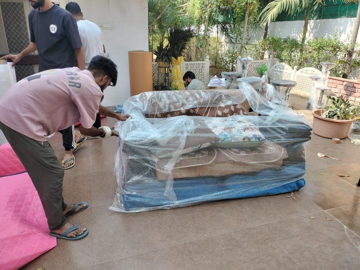 Two movers wrapping an outdoor sofa set in bubble wrap
