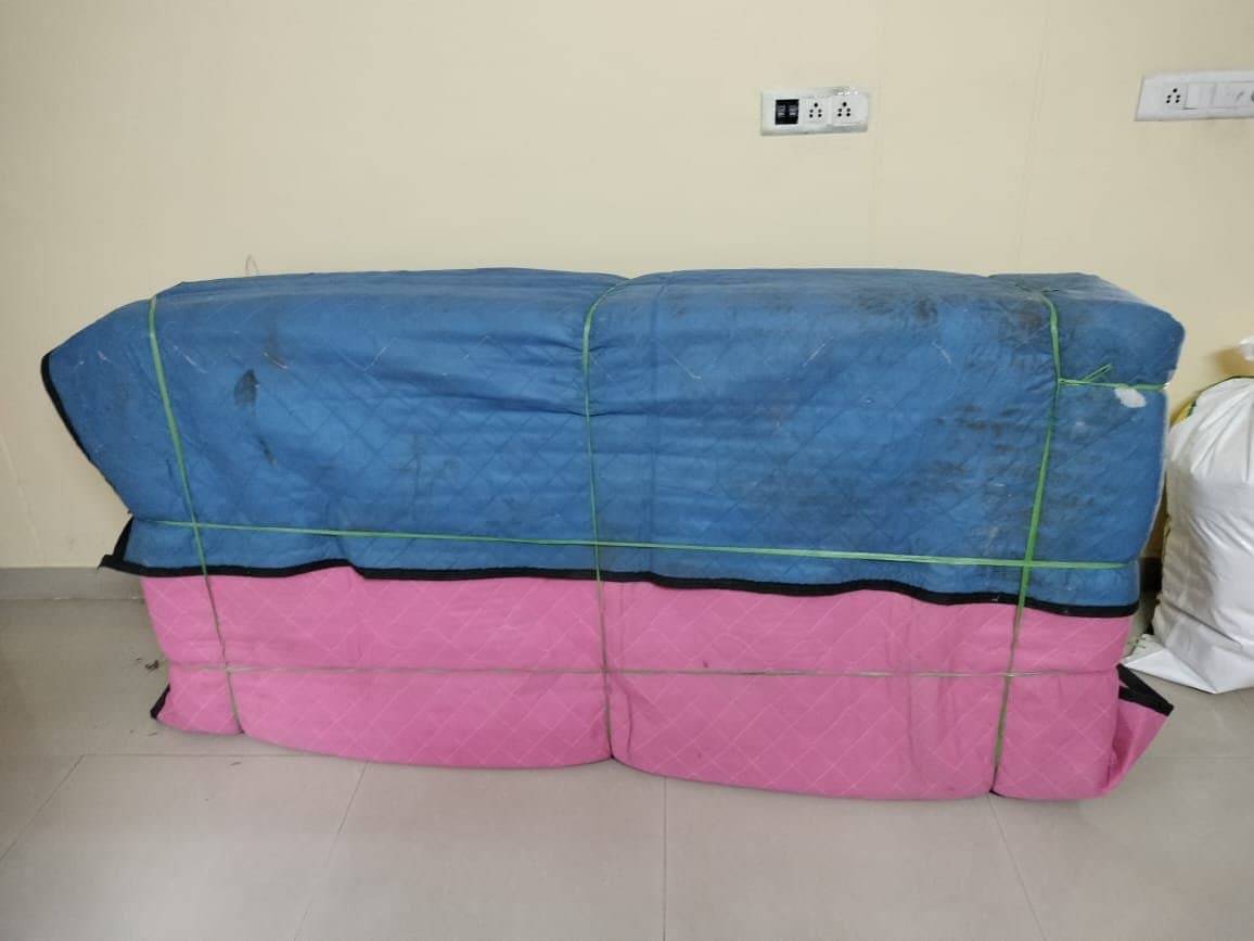 Sofa wrapped in blue and pink quilted covers and bound with straps