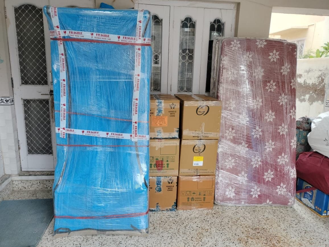 Wardrobe wrapped in blue stretch film beside fragile cartons and a rolled mattress