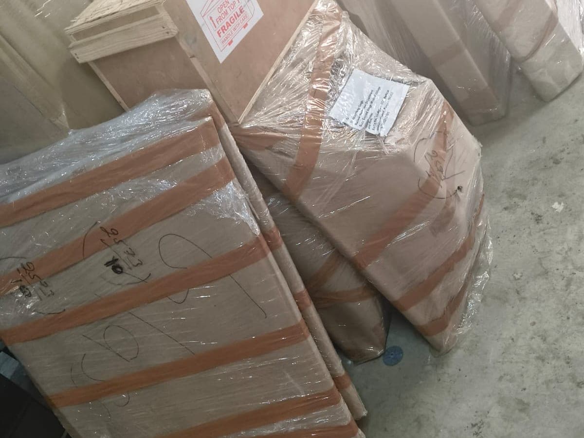 Wooden crates and wrapped furniture staged in a warehouse, one crate marked fragile and open from top
