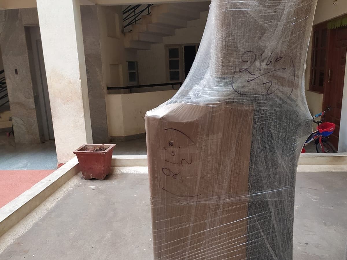 A tall piece of furniture wrapped in stretch film outside a home, marked with a handwritten inventory number
