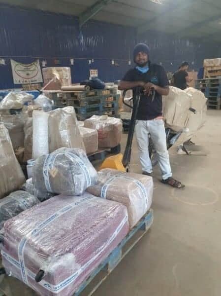 Warehouse worker with a pallet truck beside wrapped household consignments