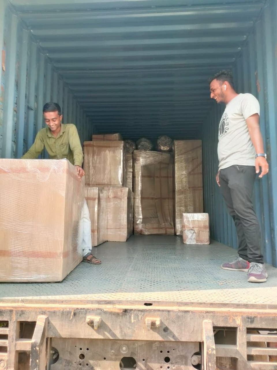 Two team members loading wrapped cartons into a container truck
