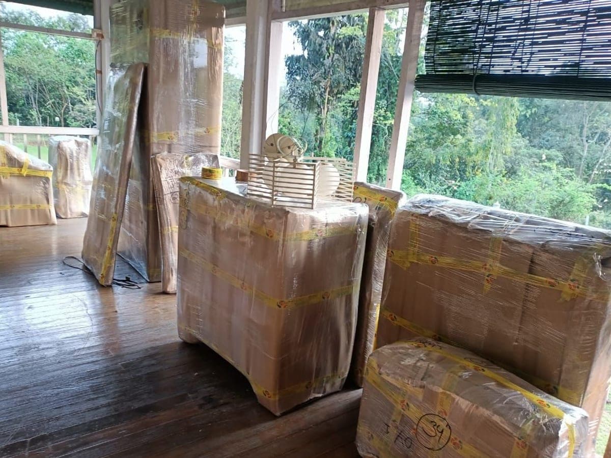 Wrapped furniture and packed cartons staged on a wooden floor beside large windows