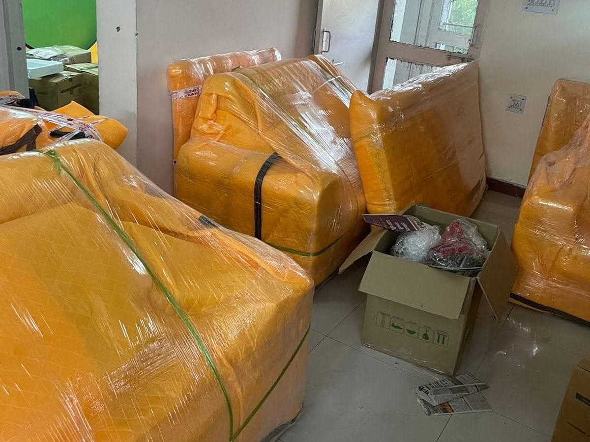 Sofas wrapped in quilted covers and stretch film in a living room, with an open carton beside them