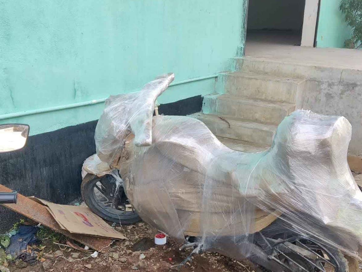 A motorcycle fully wrapped in stretch film and corrugated sheet outside a building