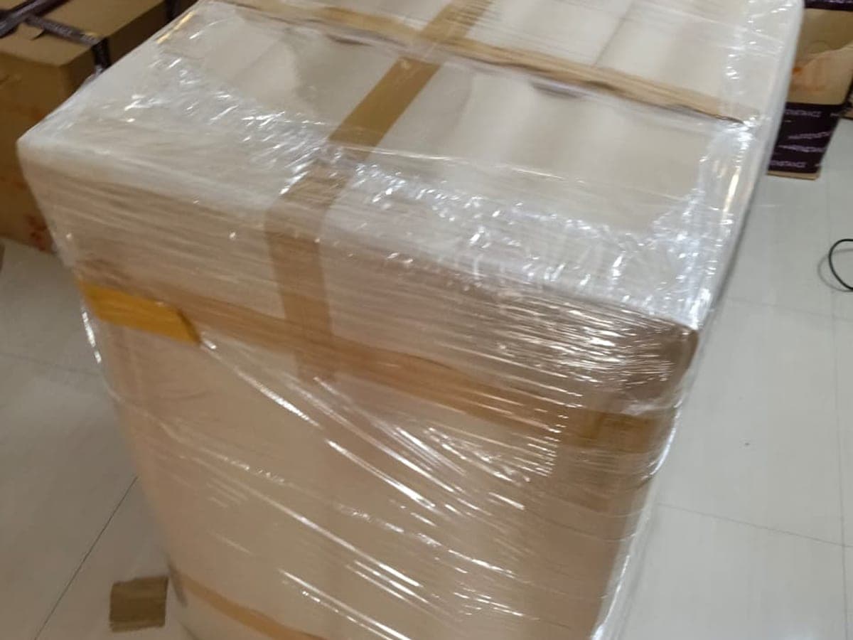 A carton sealed with tape and wrapped in stretch film on a tiled floor