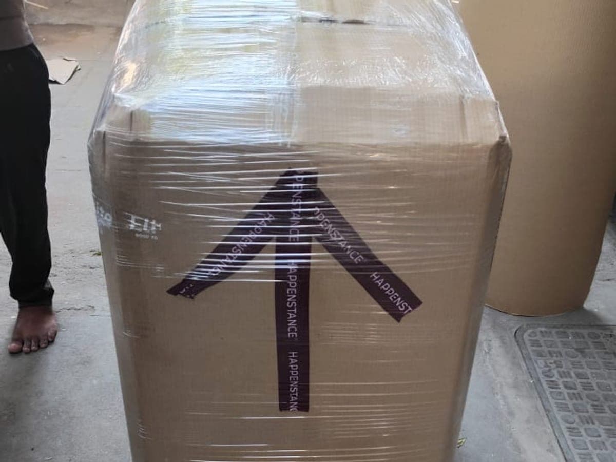 A large carton wrapped in stretch film with an arrow tape, with a scooter behind it