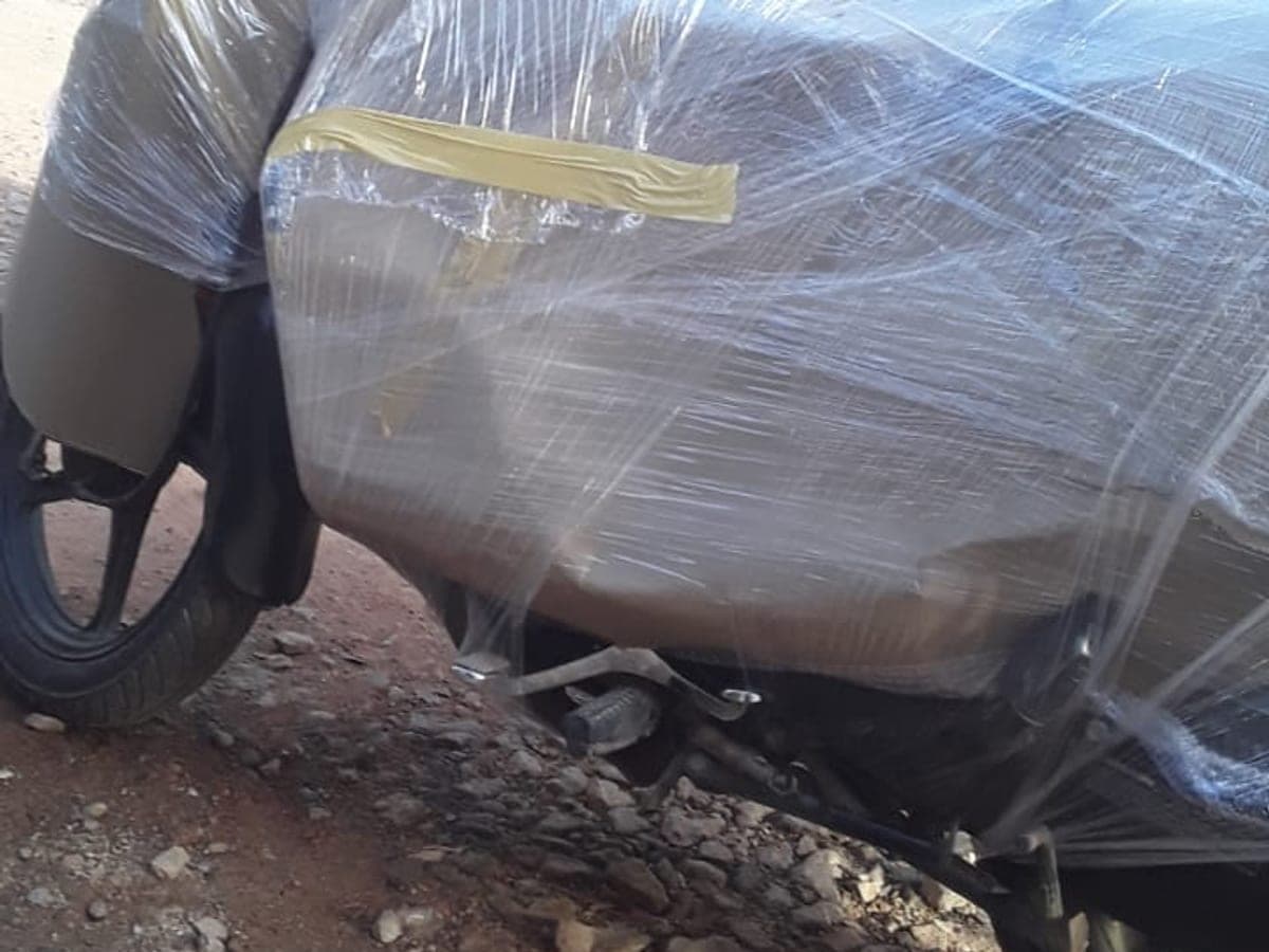 A motorcycle wrapped in stretch film and taped, being handled before loading