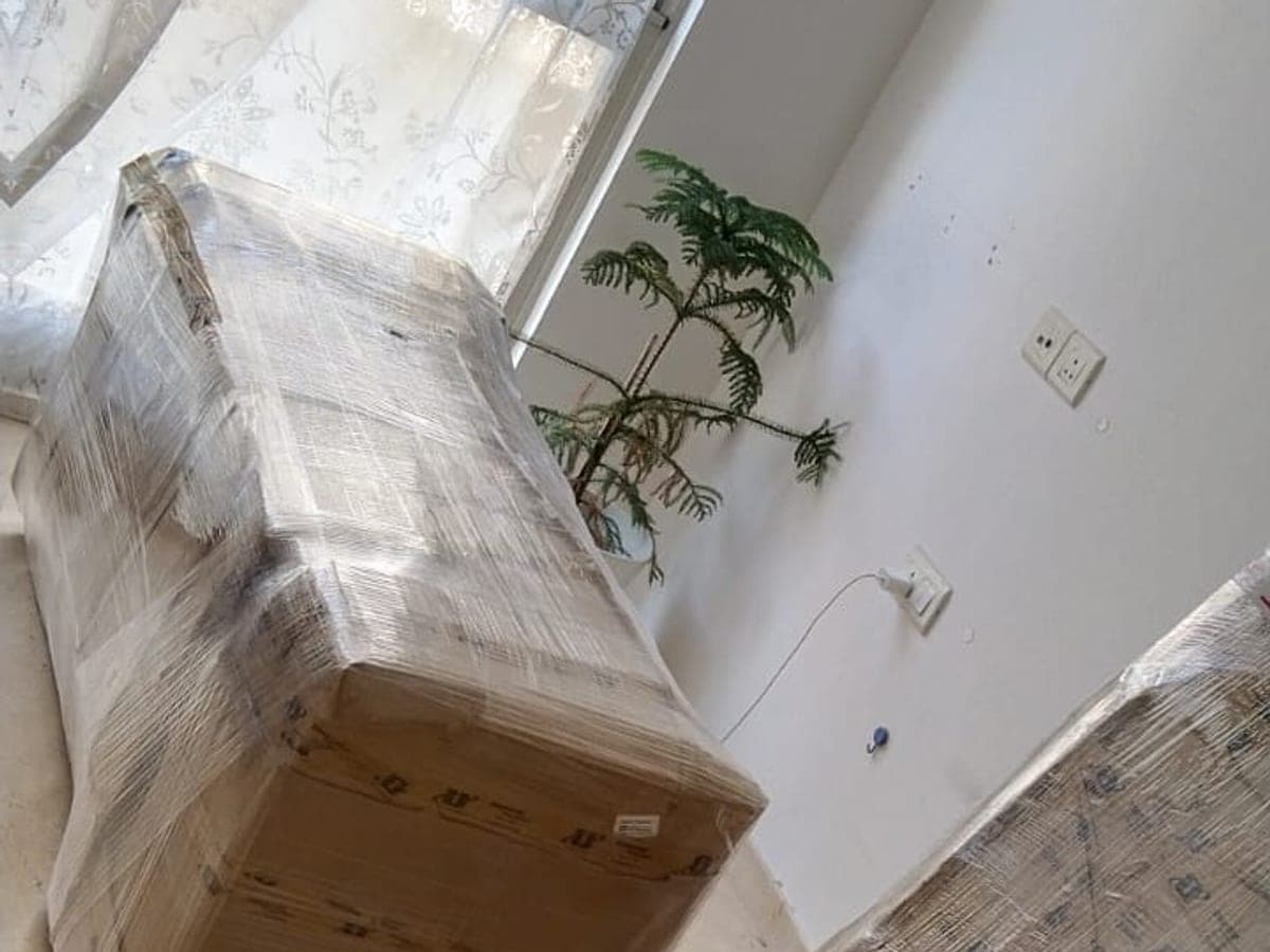 A sofa wrapped in stretch film beside a window