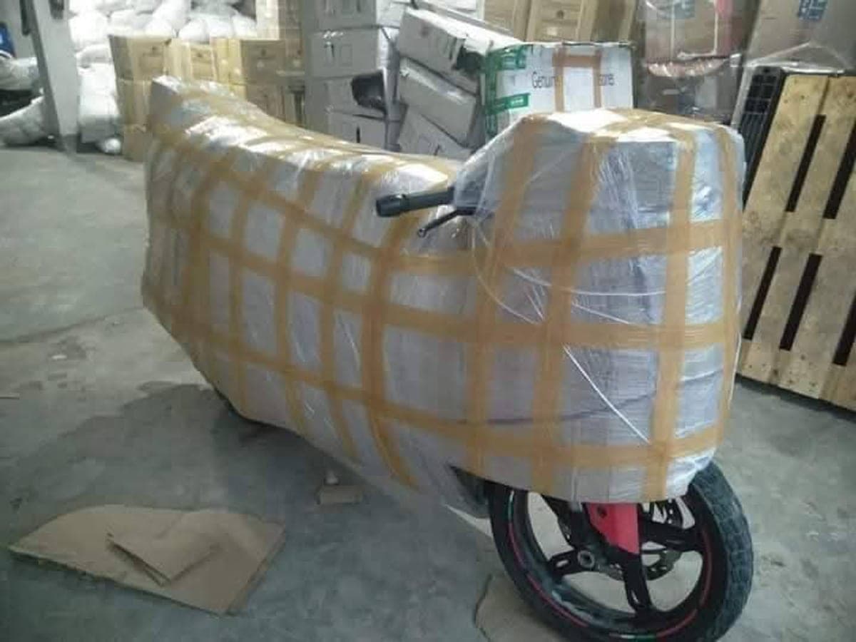 A motorcycle fully wrapped in protective sheet and strapping, waiting in a warehouse for transport