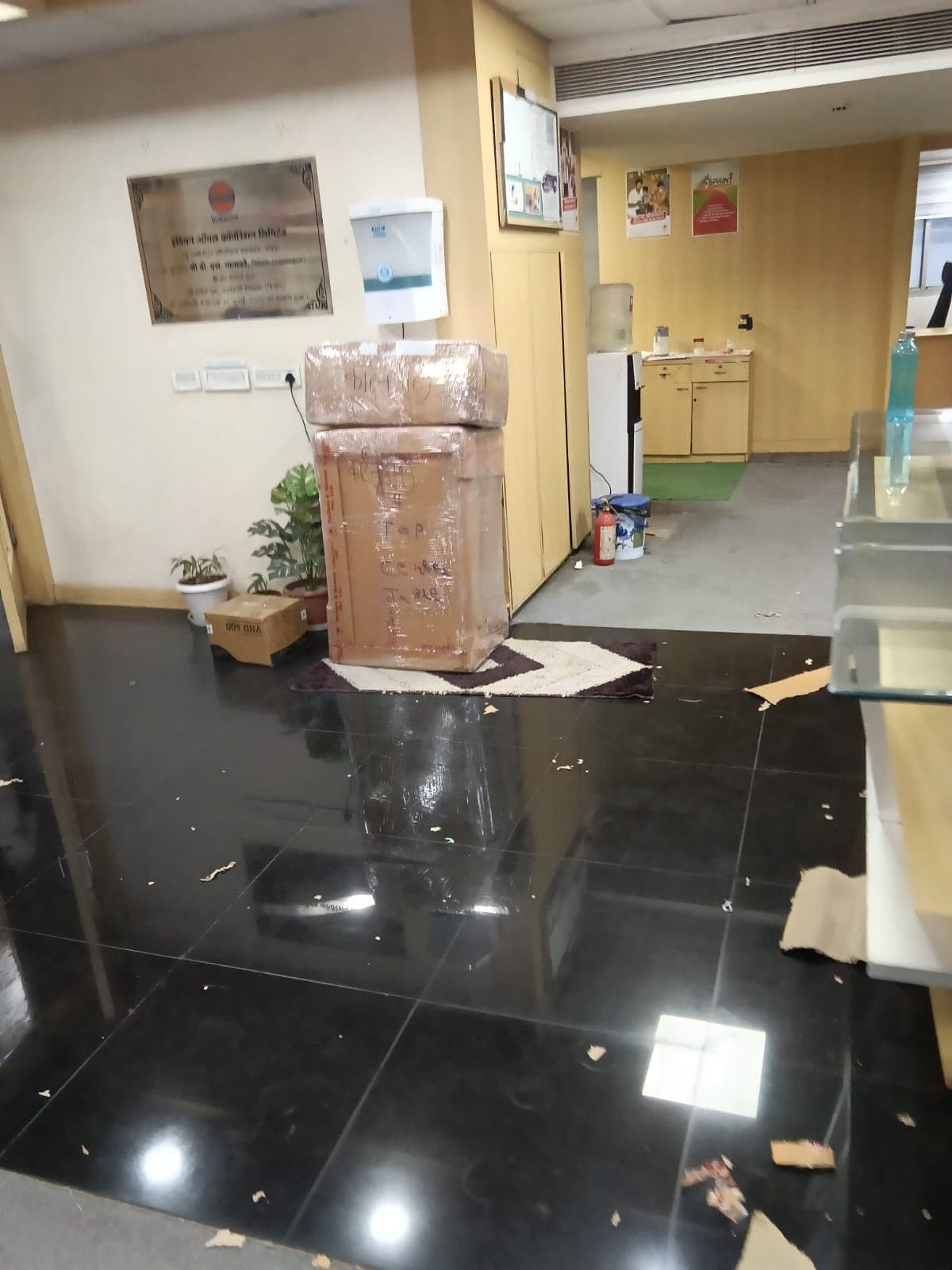 Carton wrapped in plastic and hand labeled Top of Coffee Table beside an office wall plaque