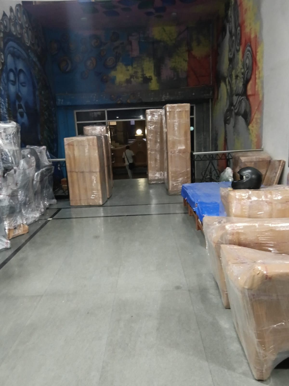 Wrapped furniture and cartons staged near a building lobby entrance with a mural on the walls