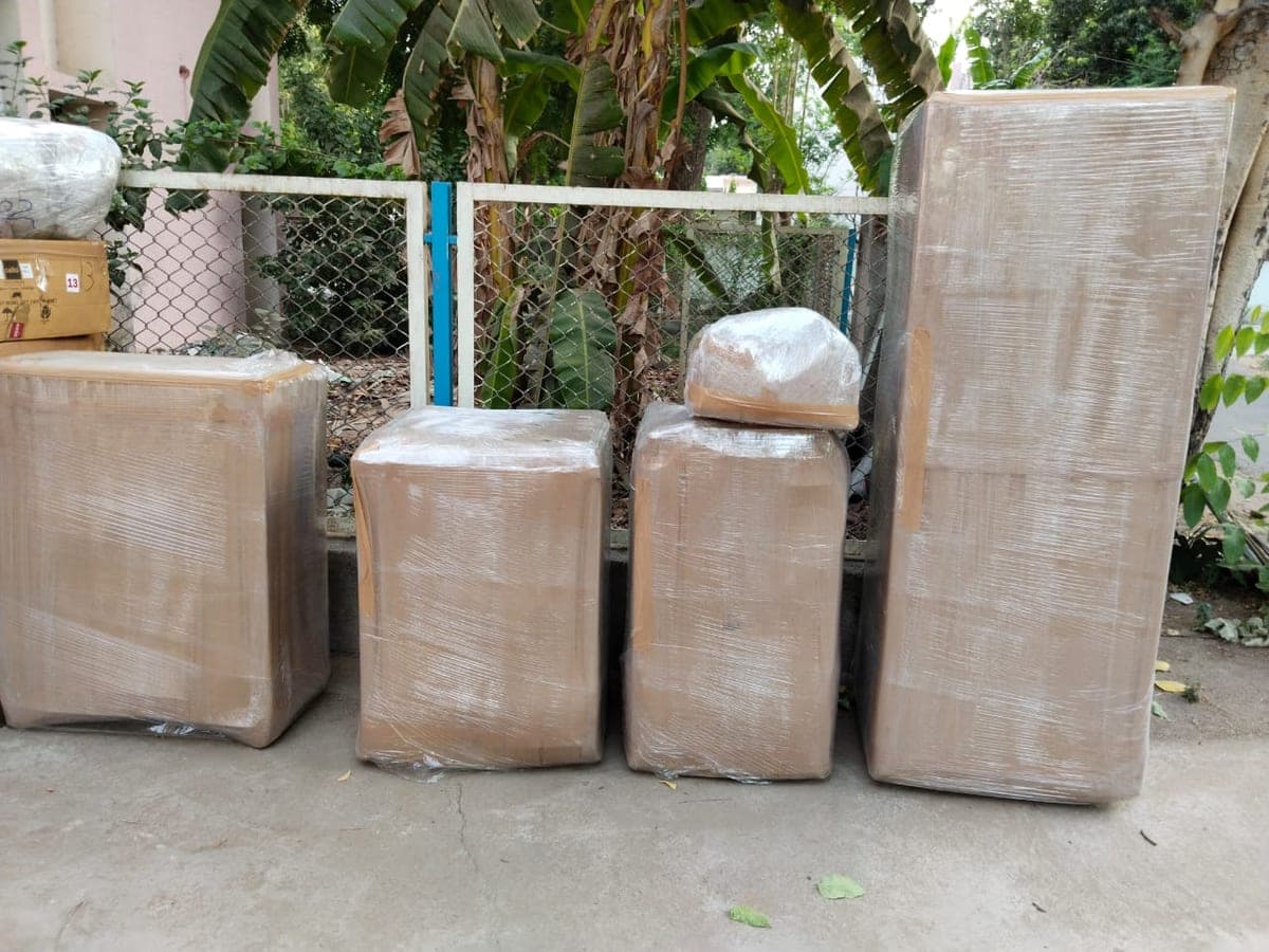 Wrapped furniture and a fridge staged outdoors before loading