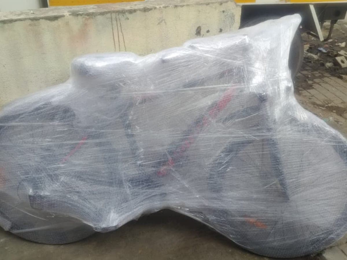 A motorcycle fully wrapped in protective bubble wrap and stretch film, staged for transport