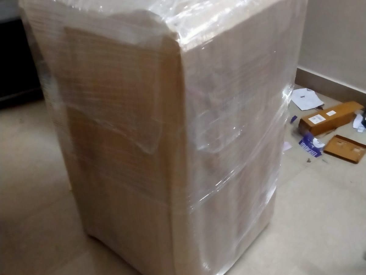 A large household item wrapped in stretch film and corrugated sheet inside a home