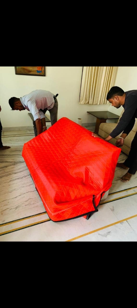 Movers fitting a padded cover over a sofa